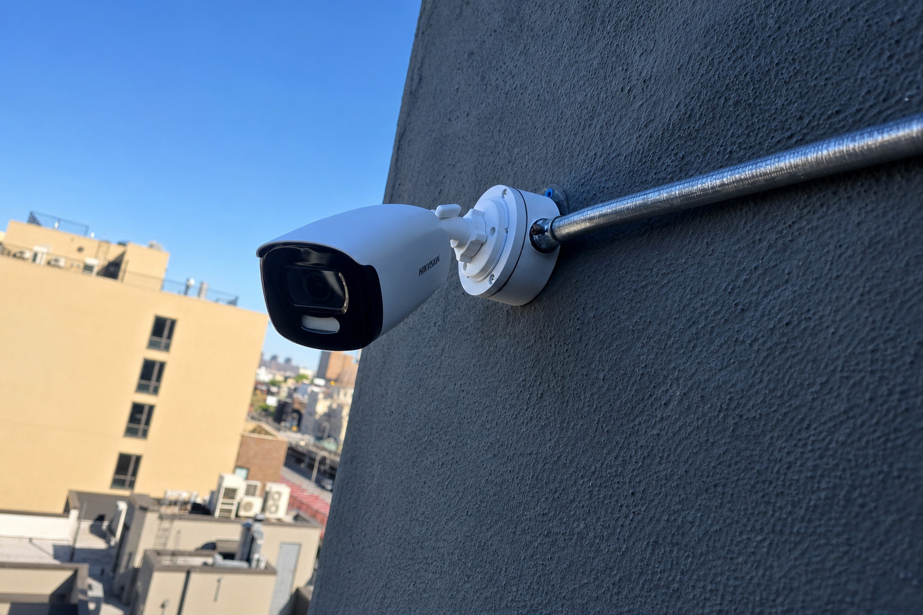 Bullet security camera mounted on a dark exterior wall with metal conduit